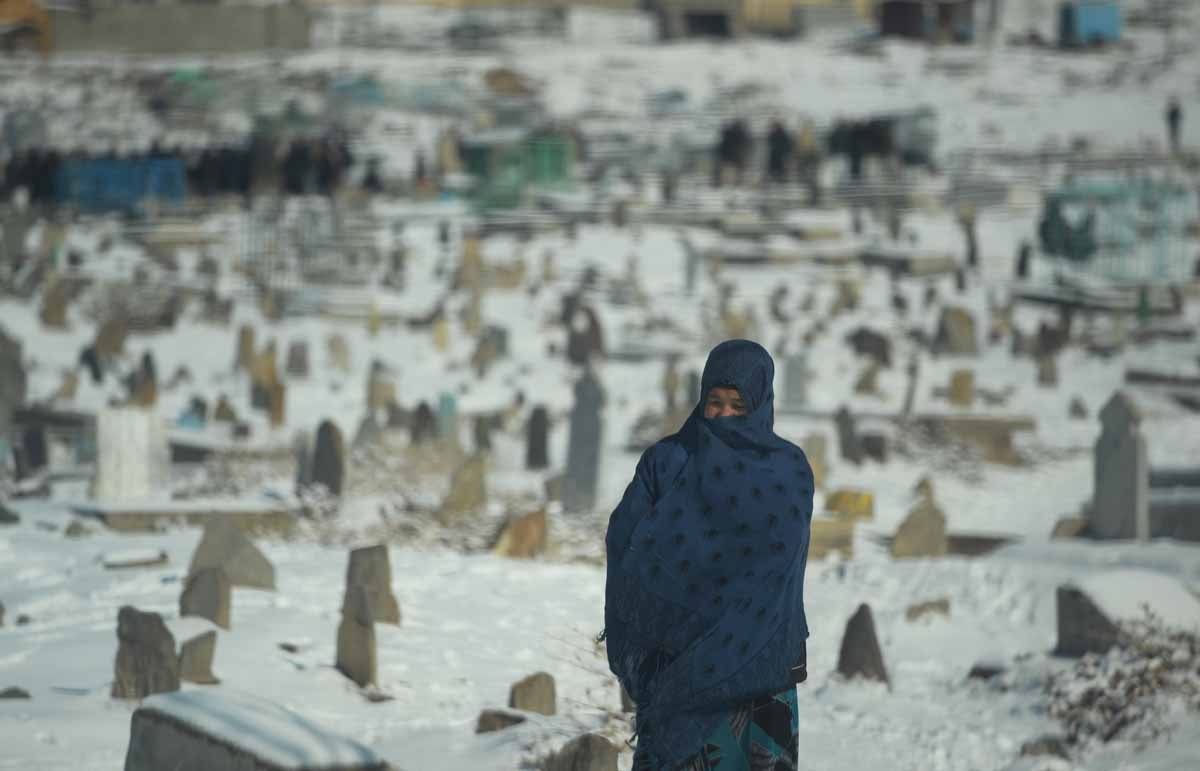 An Afghan resident wrapped in a shawl walks past a snow-covered cemetery in Kabul on January 9, 2014. As winter sets in across Central Asia, many Afghans struggle to provide adequate food and shelter for their families.