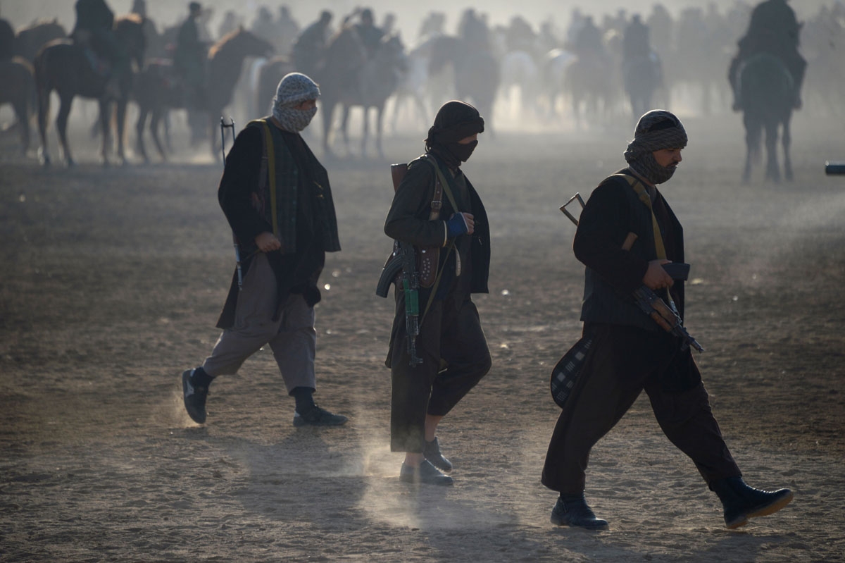 In this photograph taken on December 15, 2017, Afghan militia soldiers walk as horsemen compete in the traditional sport of Buzkashi in Mazar-i-Sharif.