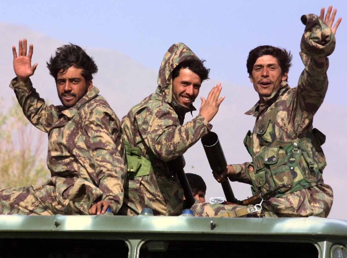 Northern Alliance soldiers wave, moving to a front line, 12 November 2001, passing by the town of Baghram, some 25 kms north from Kabul.