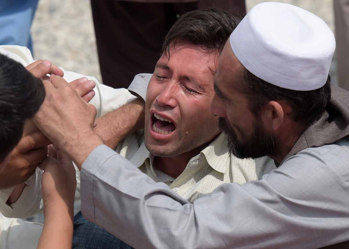 A relative (C) is comforted as he weeps alongside unseen shoes and other belongings of those who were killed in the twin suicide attack, at a mosque in Kabul on July 24, 2016