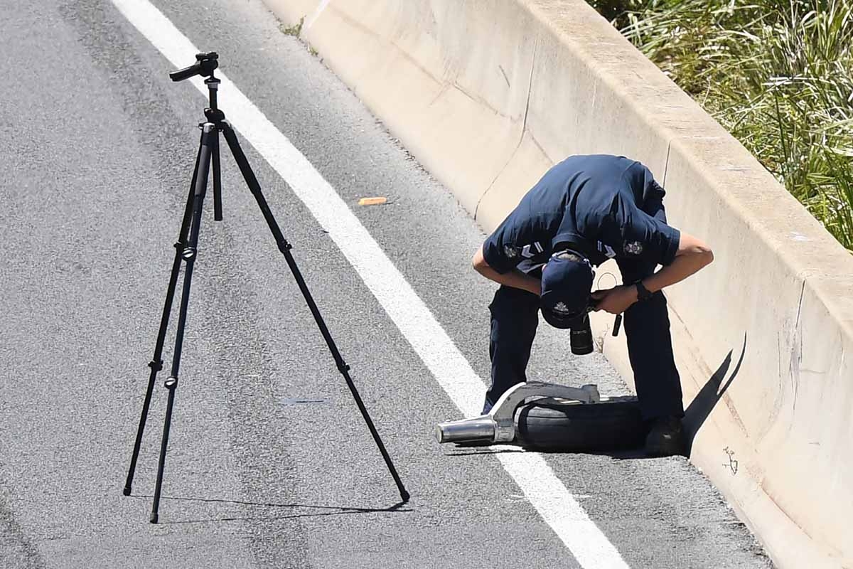 A policeman photographs a plane wheel on the freeway of a Beechcraft plane after it crashed into a shopping centre just after take-off from the Essendon airport in Melbourne on February 21, 2017.