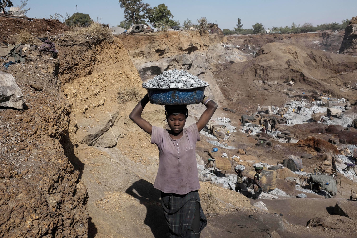 A young girl carries a bucket full of crushed stones at a quarry in Ouagadougou where adults and children work on December 17, 2015.