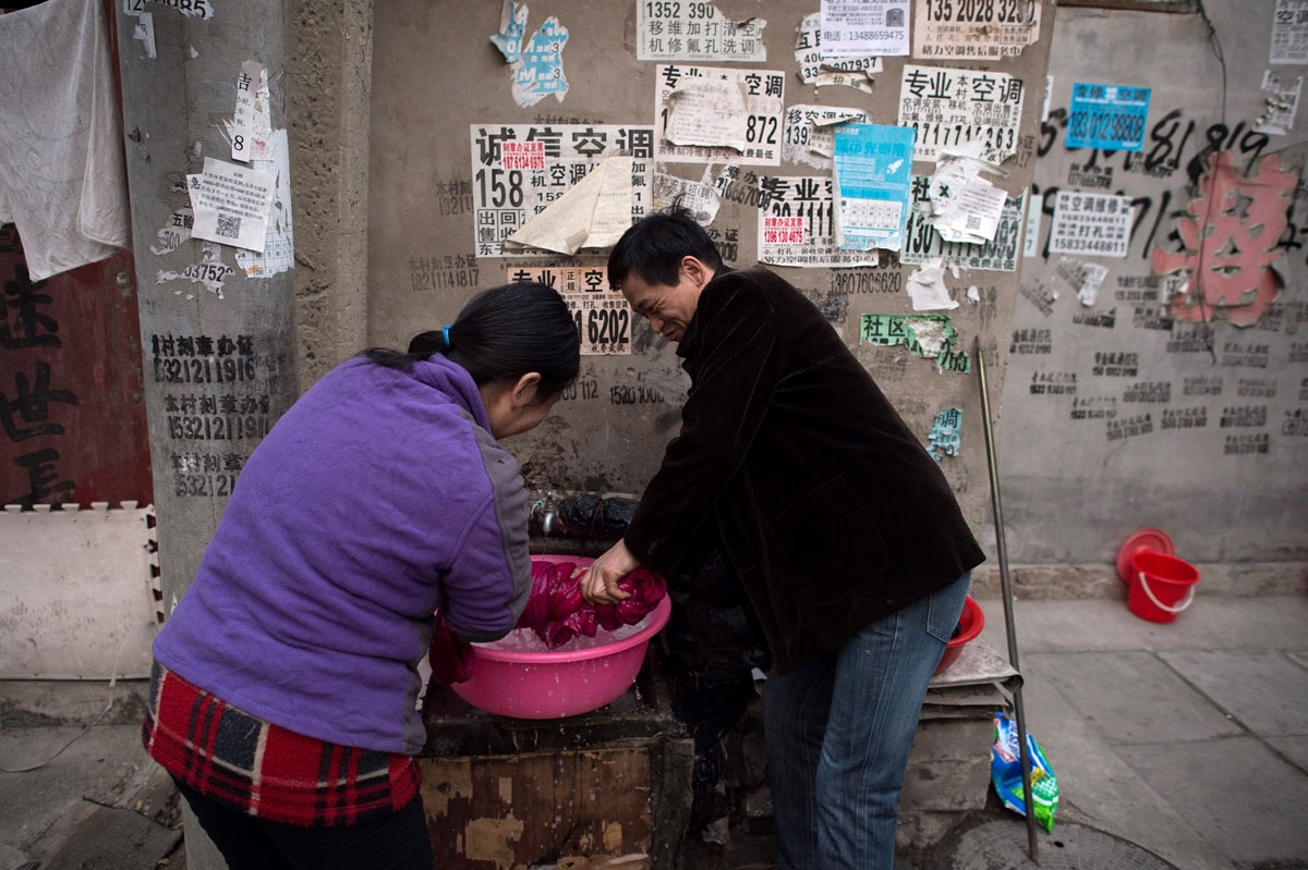 This picture taken on February 15, 2017 shows a man helping a woman to wring a coat dry in the Heiqiaocun migrant village in Beijing.