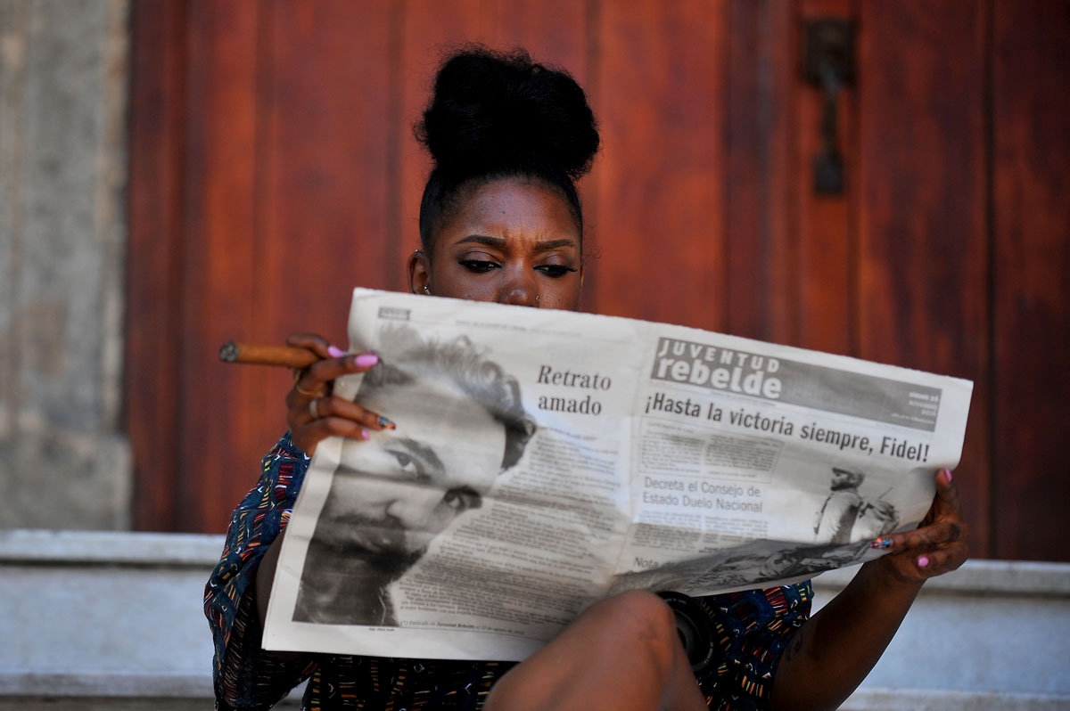 A woman smokes a cigar as she reads the newspaper in a street of Havana, on November 26, 2016, the day after Cuban revolutionary leader Fidel Castro died aged 90.