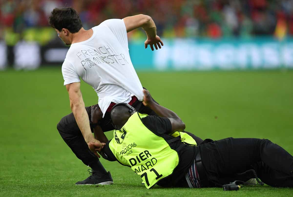 A steward grabs a supporter entering the pitch during the Euro 2016 final football match between Portugal and France at the Stade de France in Saint-Denis, north of Paris, on July 10, 2016. / AFP PHOTO / PATRIK STOLLARZ A steward grabs a supporter entering the pitch during the Euro 2016 final football match between Portugal and France at the Stade de France in Saint-Denis, north of Paris, on July 10, 2016. / AFP PHOTO / PATRIK STOLLARZ