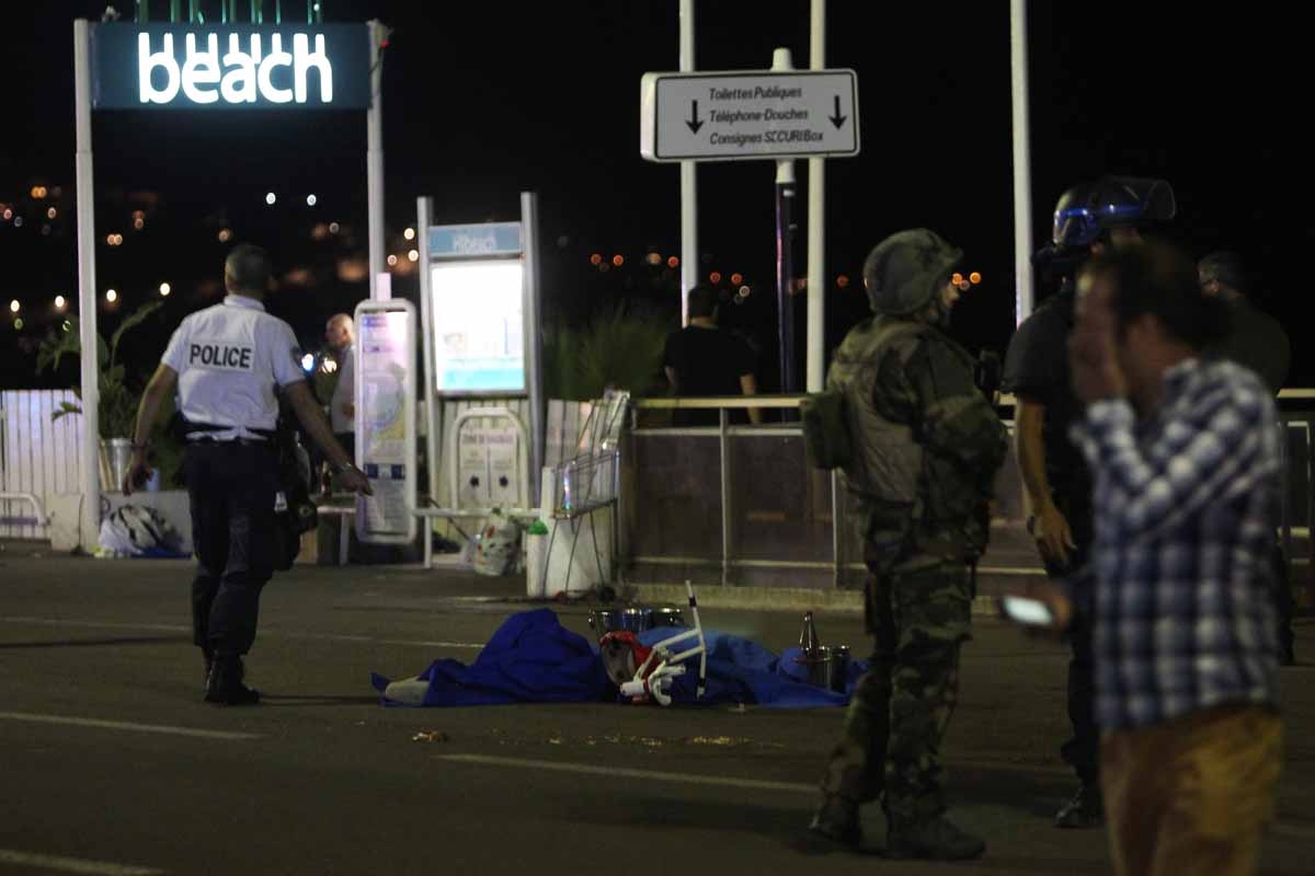 A police officer stands next to a dead body covered with a blue sheet on the Promenade des Anglais seafront in the French Riviera town of Nice on July 15, 2016, after a van drove into a crowd watching a fireworks display. A police officer stands next to a dead body covered with a blue sheet on the Promenade des Anglais seafront in the French Riviera town of Nice on July 15, 2016, after a van drove into a crowd watching a fireworks display.
