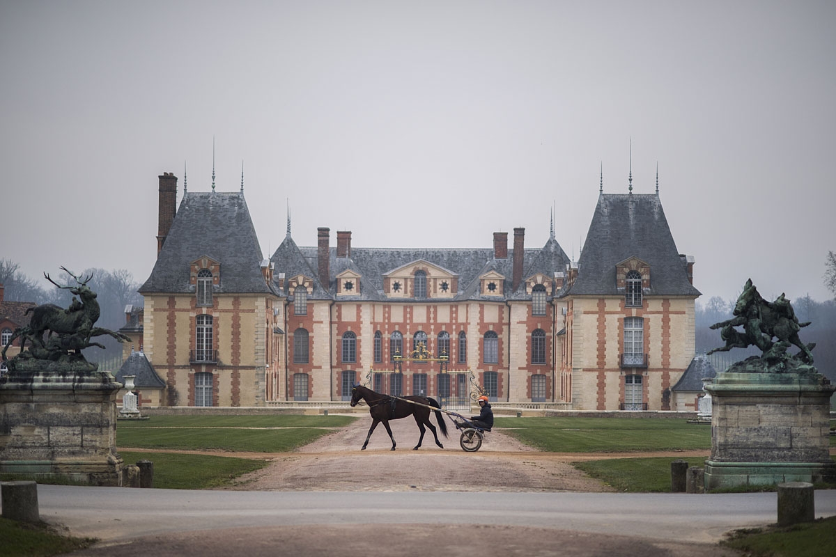 A horse and its driver walk past the castle of Grobois at the equestrian training center of Grosbois in Marolles-en-Brie, on December 2, 2016.