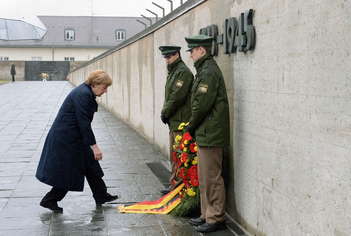 German Chancellor Angela Merkel bows to adjust the ribbons of a wreath laid in her name in front of the International Memorial of former Nazi concentration camp of Dachau, southwestern Germany, during a ceremony to mark 70 years since it was liberated by