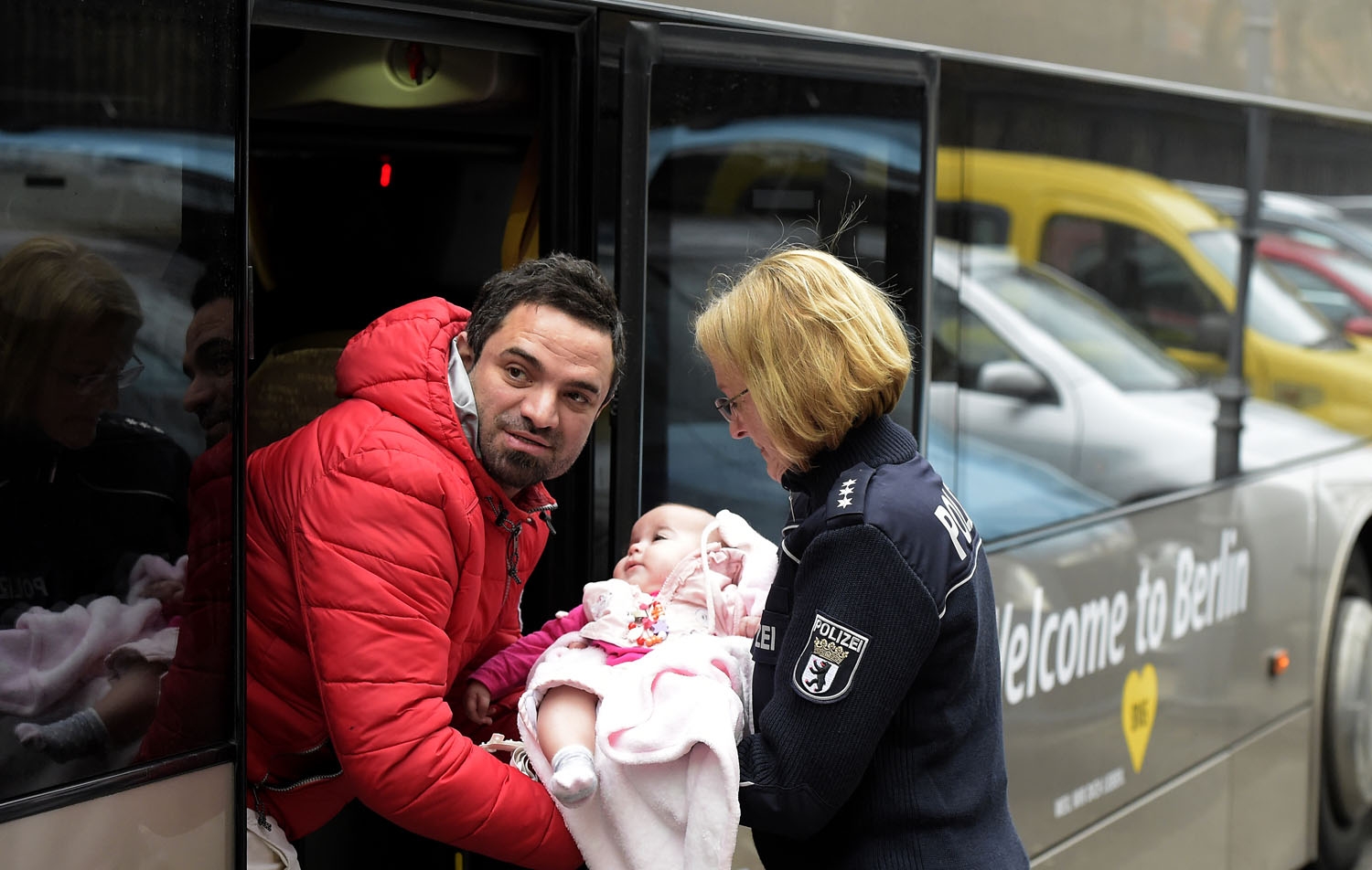 A German police woman helps a man carrying a baby into a bus outside the registration office of the State Office of Health and Social Affairs (LAGeSo) in Berlin on March 11, 2016. / AFP PHOTO / TOBIAS SCHWARZ A German police woman helps a man carrying a baby into a bus outside the registration office of the State Office of Health and Social Affairs (LAGeSo) in Berlin on March 11, 2016. / AFP PHOTO / TOBIAS SCHWARZ