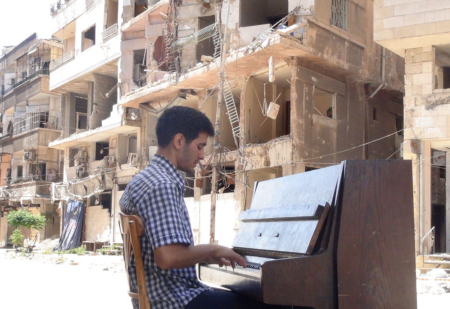 Ayham al-Ahmed, a resident of Damascus' Yarmuk Palestinian refugee camp, plays the piano in the middle of the street near destroyed buildings, on June 26, 2014 Ayham al-Ahmed, a resident of Damascus' Yarmuk Palestinian refugee camp, plays the piano in the middle of the street near destroyed buildings, on June 26, 2014