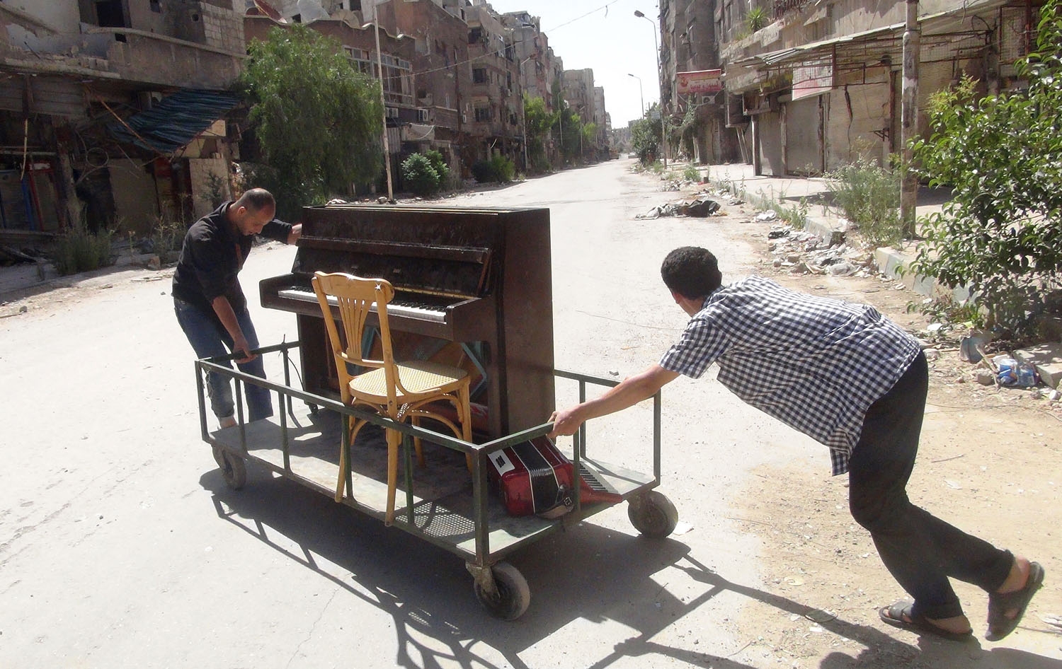 Ayham al-Ahmed (R), a resident of Damascus' Yarmuk Palestinian refugee camp, is helped by friends to push his piano in the middle of the street on June 26, 2014 Ayham al-Ahmed (R), a resident of Damascus' Yarmuk Palestinian refugee camp, is helped by friends to push his piano in the middle of the street on June 26, 2014