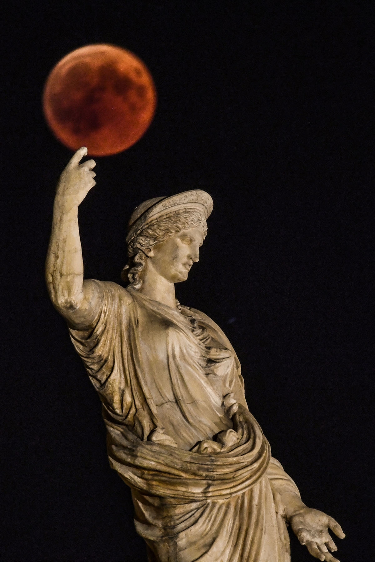 A picture shows the full moon during a blood moon eclipse beside a statue of the ancient Greek goddess Hera in central Athens on July 27, 2018.