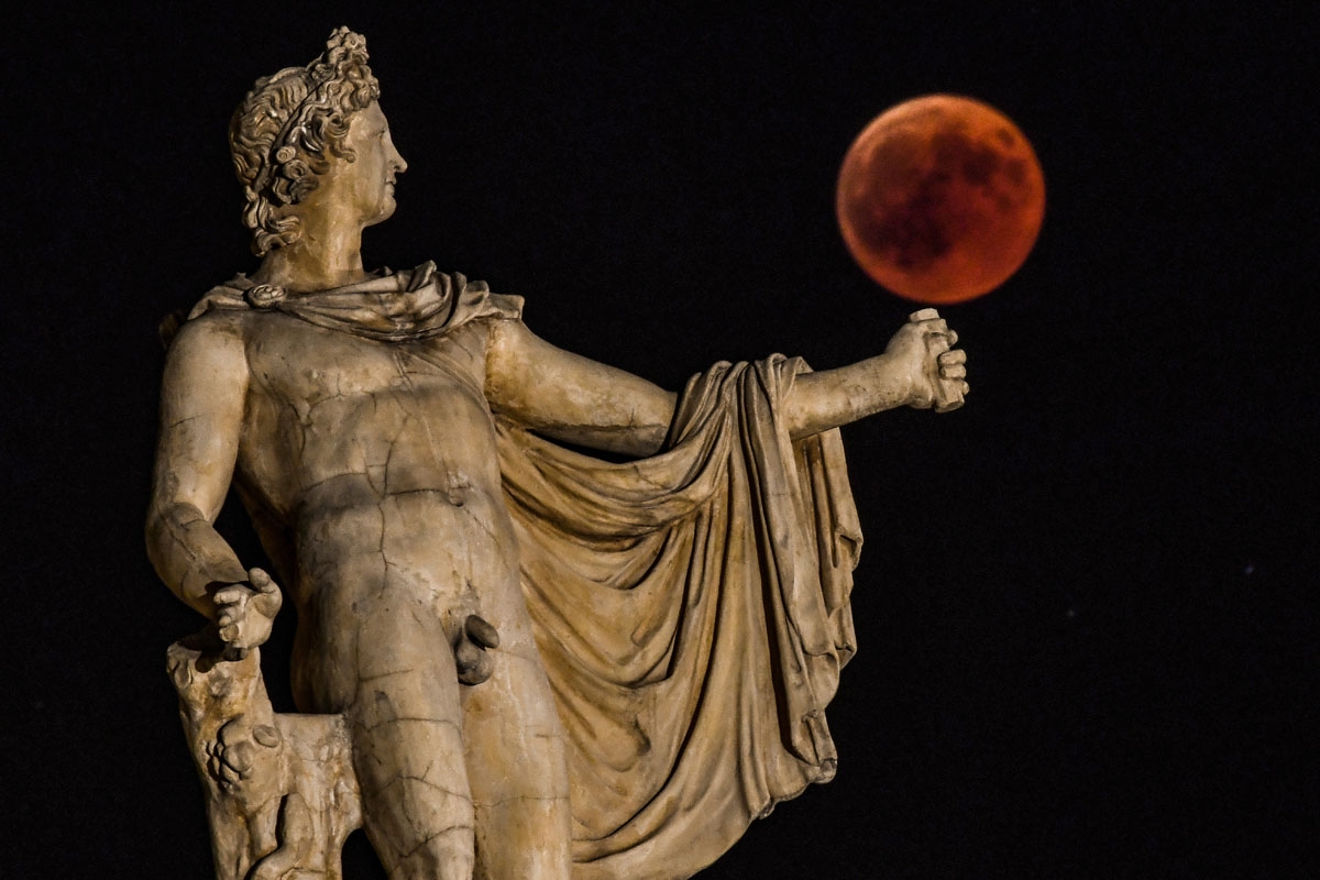 A picture shows the full moon during a blood moon eclipse beside a statue of the ancient Greek god Apollo in central Athens on July 27, 2018.