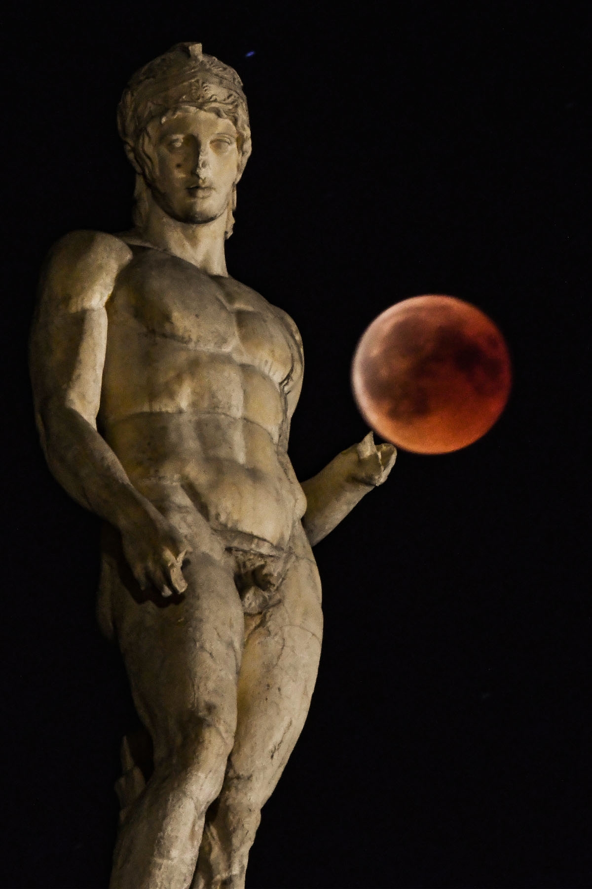 A picture shows the full moon during a blood moon eclipse beside a statue of ancient Greek god Ares in central Athens on July 27, 2018.