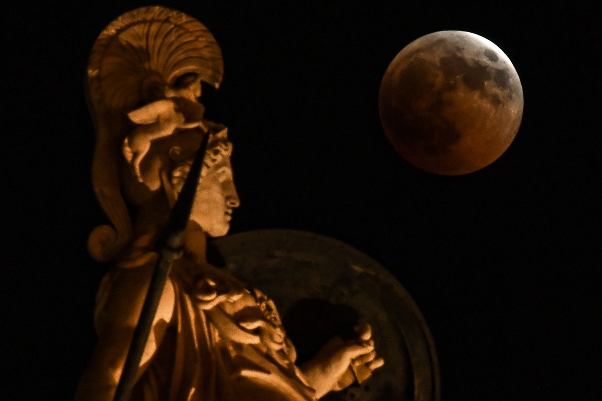 A picture shows the full moon during a blood moon eclipse beside a statue of ancient Greek goddess Athena in central Athens on July 27, 2018.