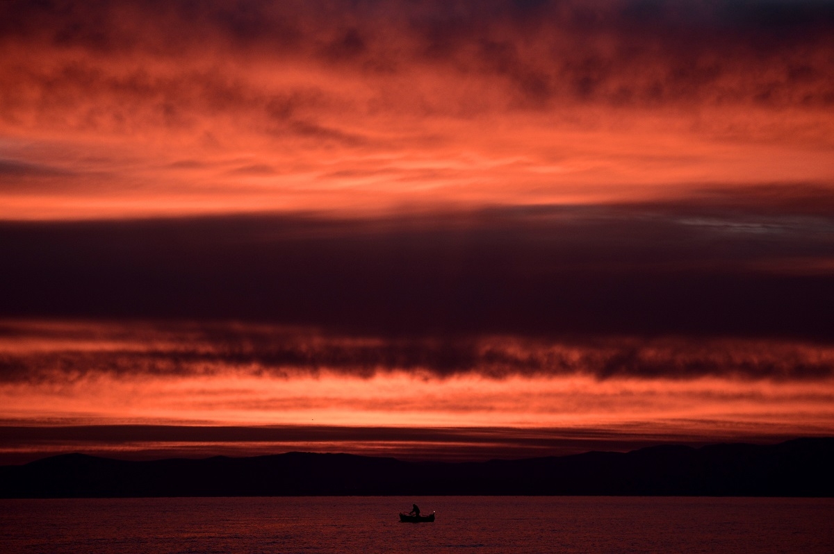 A fisherman stands on his boat during sunrise off Mytilene, on the northern Greek island of Lesbos, on February 23, 2016.