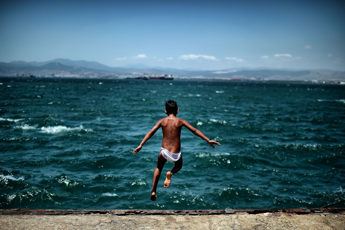 A young refugee jumps into the sea next to the refugee camp of Skaramangas in Athens on June 24, 2016.