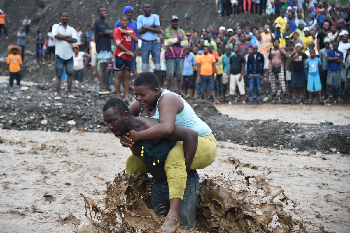 A man carries a woman across a river at Petit Goave where a bridge collapsed during the rains of the Hurricane Matthew, southwest of Port-au-Prince, October 5, 2016. A man carries a woman across a river at Petit Goave where a bridge collapsed during the rains of the Hurricane Matthew, southwest of Port-au-Prince, October 5, 2016.