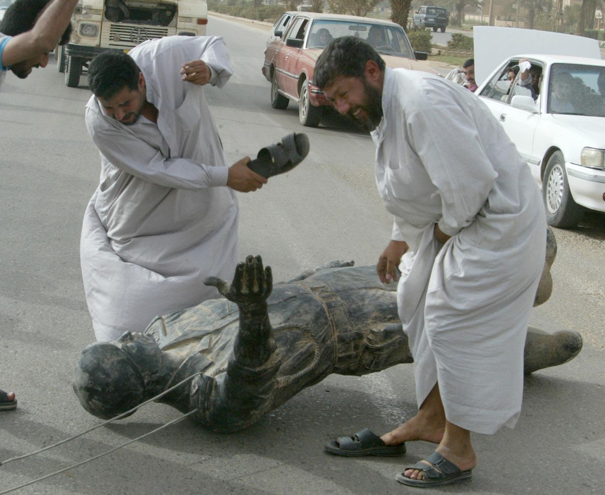 Iraqis hit a statue of Saddam Hussein with their sandals in Baghdad 09 April 2003 after it was pulled down as US tanks rolled into the heart of the Iraqi capital