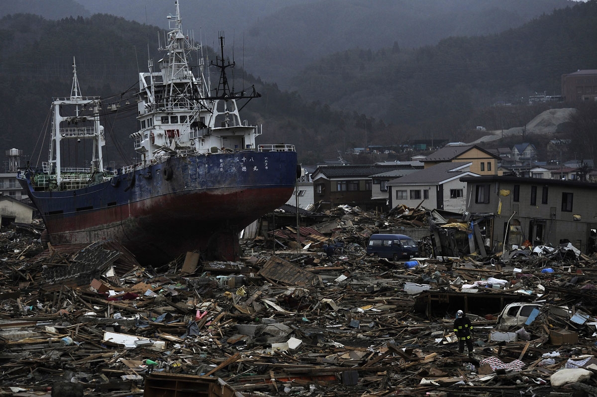 A Japanese firefighter (R) walks past a boat pushed inland by the March 11 tsunami in Kesennuma in Miyagi prefecture on March 20, 2011.