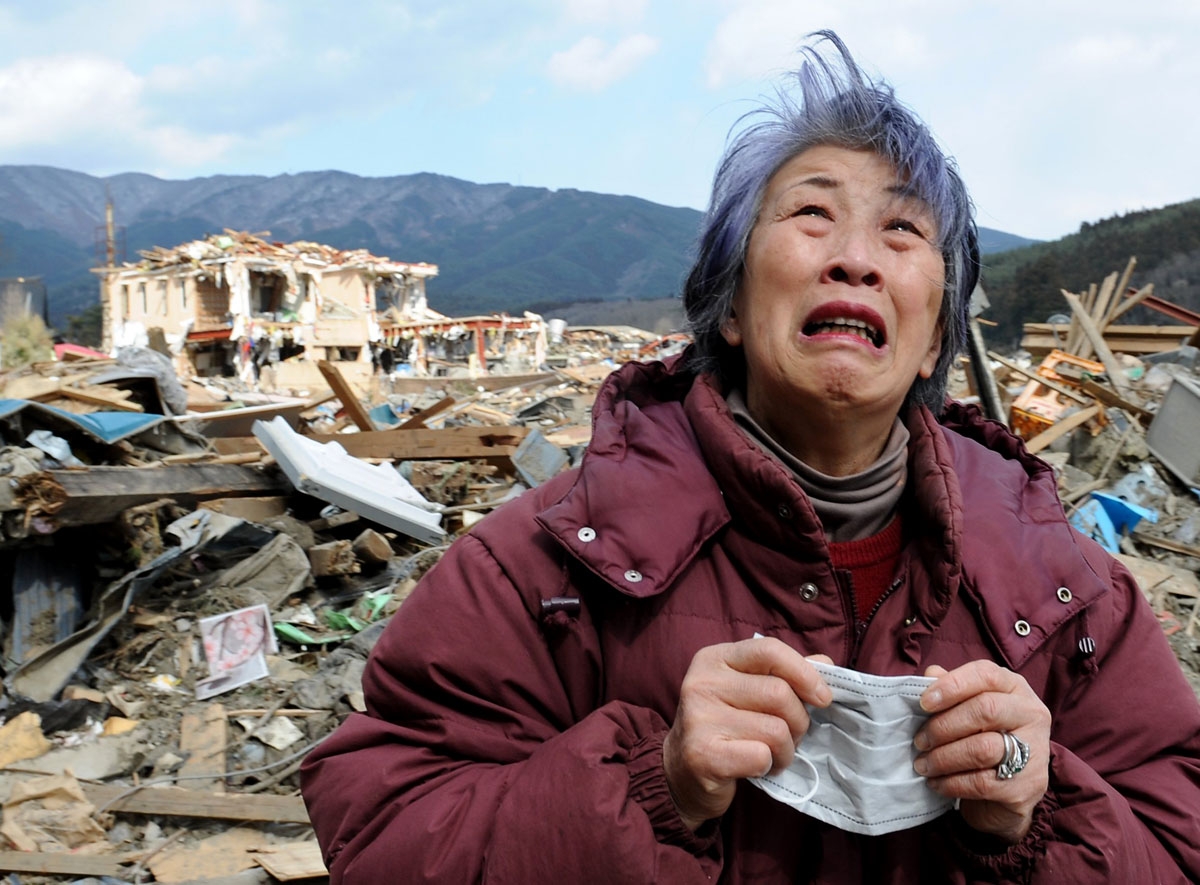 An elderly woman cries in front of a destroyed building in the devastated town of Rikuzentakata in Iwate prefecture on March 19, 2011, eight days after a massive 9.0 magnitude earthquake and tsunami hit the northeastern coast of Japan's main island of Hon