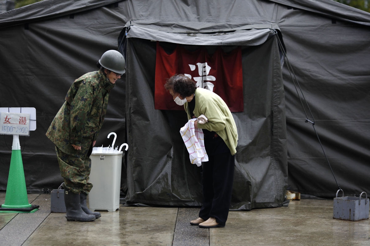 An elderly woman (R) gives thanks to an officer of the Self-Defense Force after she bathed at a temporary hot bath at a shelter in Koryama in Fukushima prefecture on March 21, 2011.