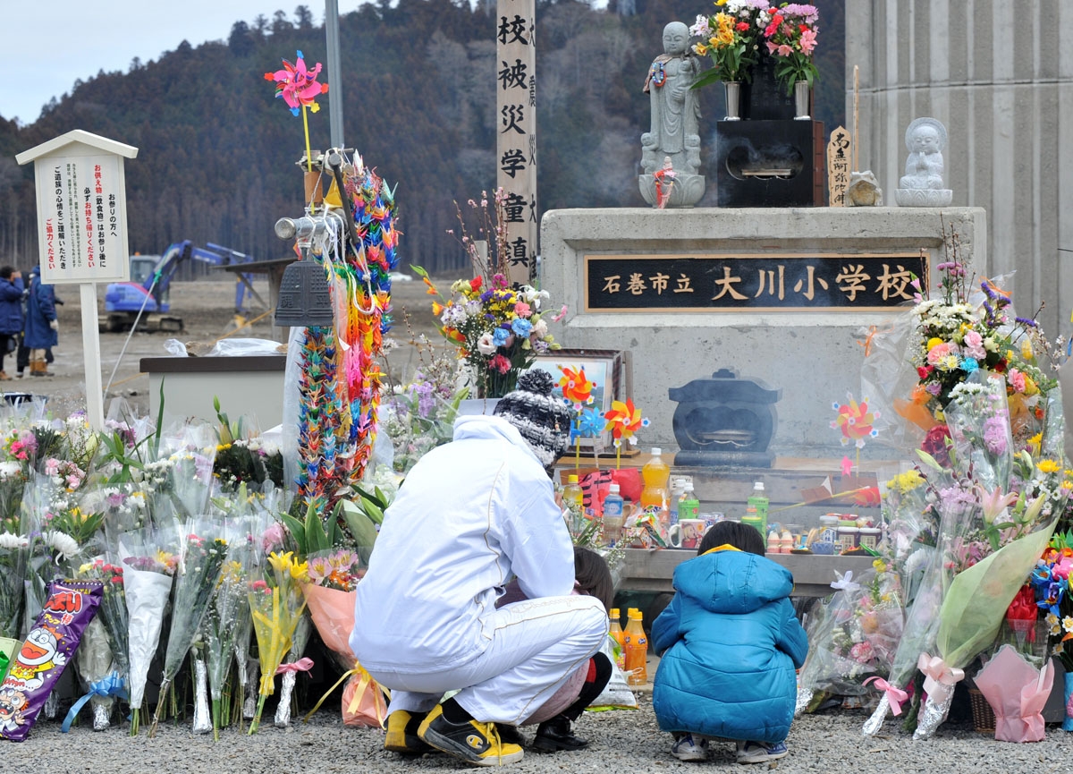 A family pray for 74 elementary school children and 10 teachers who lost their lives in the March 11 earthquake and tsunami, at a memorial in front of the Okawa elementary school during the first year anniversary of the disaster in Ishinomaki, Miyagi pref