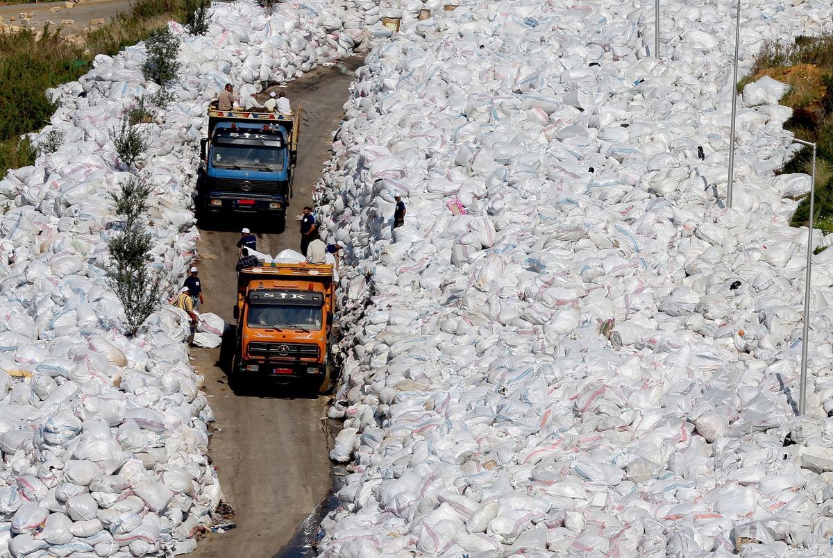 Rubbish trucks drive between a built up pile of waste on a street in Beirut's northern suburb of Jdeideh on February 25, 2016