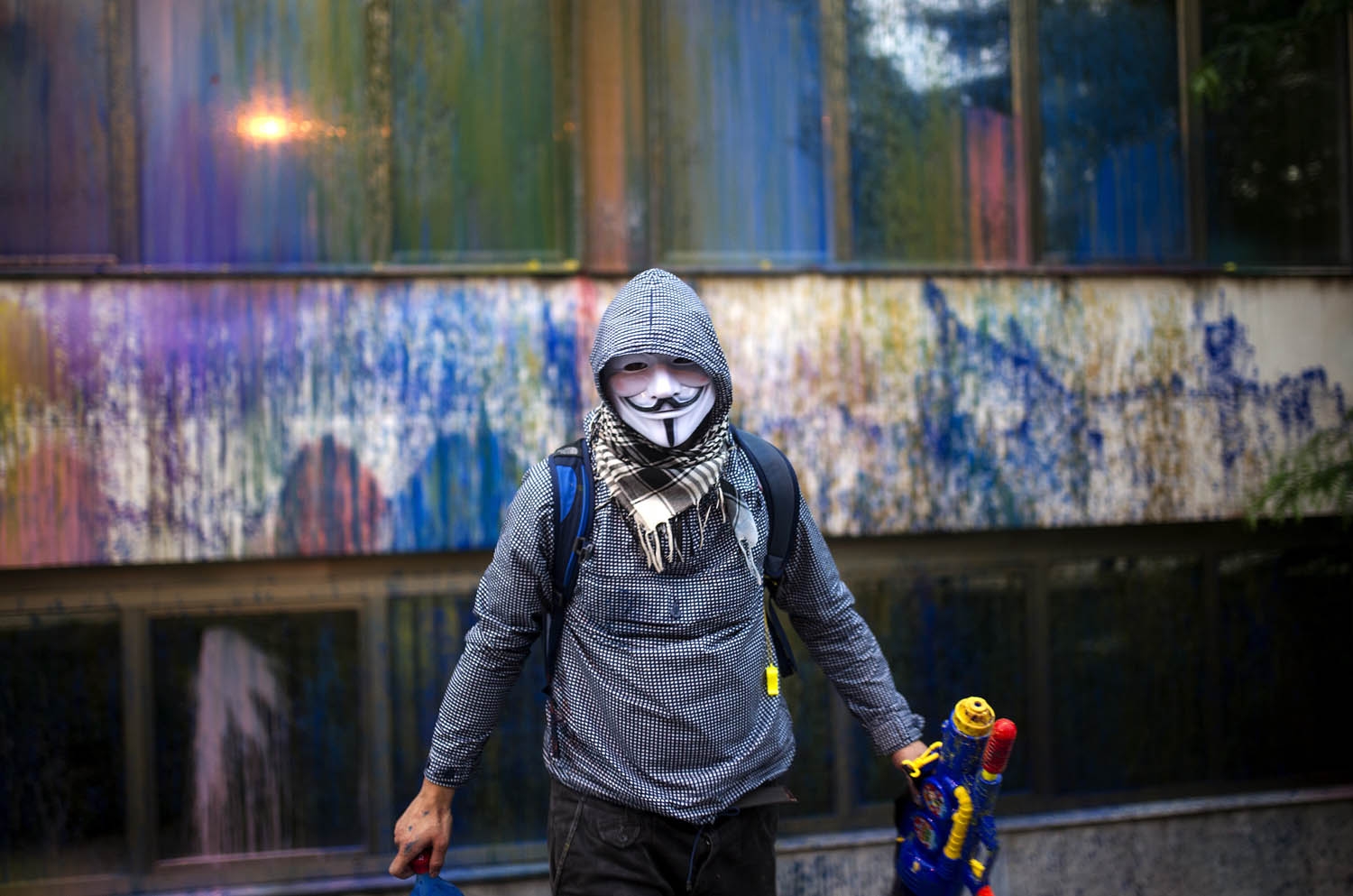 A protester wearing a Guy Fawkes mask, sprays paint with toy water gun on the facade of the Macedonia's Public Revenue Office headquarters on May 10, 2016 in Skopje