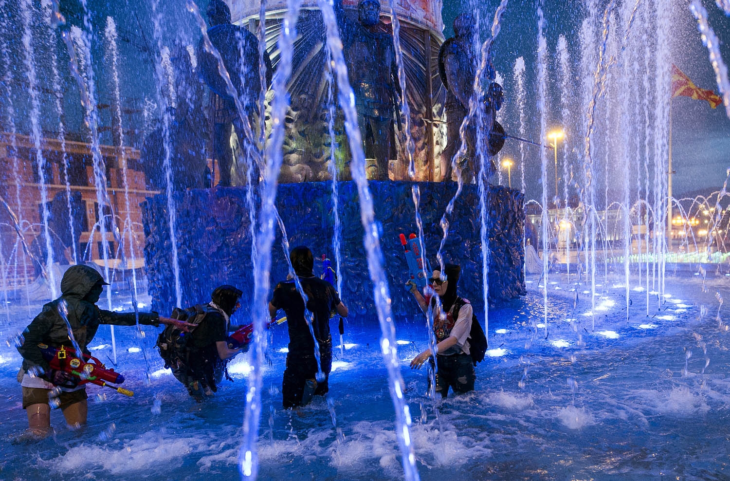 Protestors wearing masks use water guns to spray coloured paint on The Alexander the Great Fountain during an anti-government protest in Skopje on June 3, 2016, in a series of protests dubbed Colourful Revolution