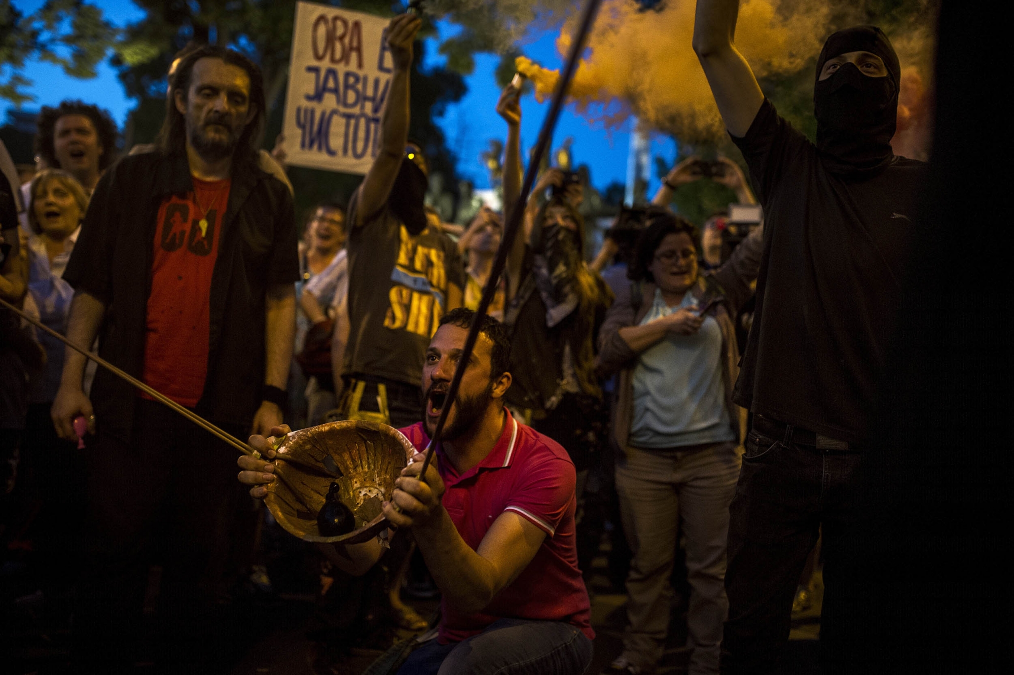 A hooded protestor uses an improvised slingshot to throw a balloon with colored paint on the Parliament building while others hold colored smoke cartridges, during an anti-government protest in Skopje on May 27, 2016