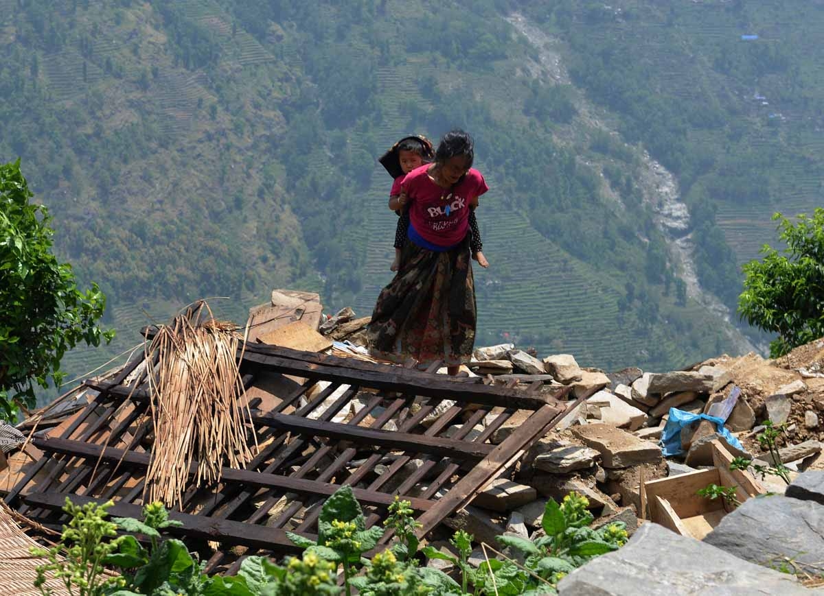 A Nepalese resident carries a child on her back as she walks past damaged homes in the village of Ebi in Dhading district some 60kms north-west of Kathmandu on May 11, 2015. A Nepalese resident carries a child on her back as she walks past damaged homes in the village of Ebi in Dhading district some 60kms north-west of Kathmandu on May 11, 2015.