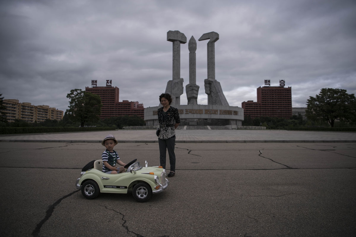 In a photo taken on July 6, 2016 a woman stands before a child driving an electric toy car at the Monument to the Founding of the Workers Party of Korea, in Pyongyang