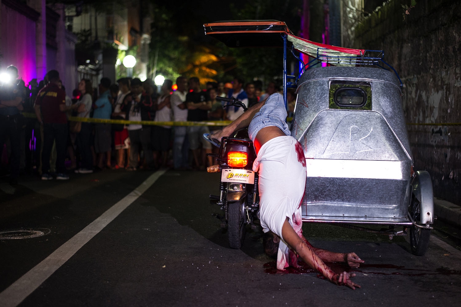 Bystanders watch the dead body of a tricycle driver shot by gunmen in Manila on July 22, 2016