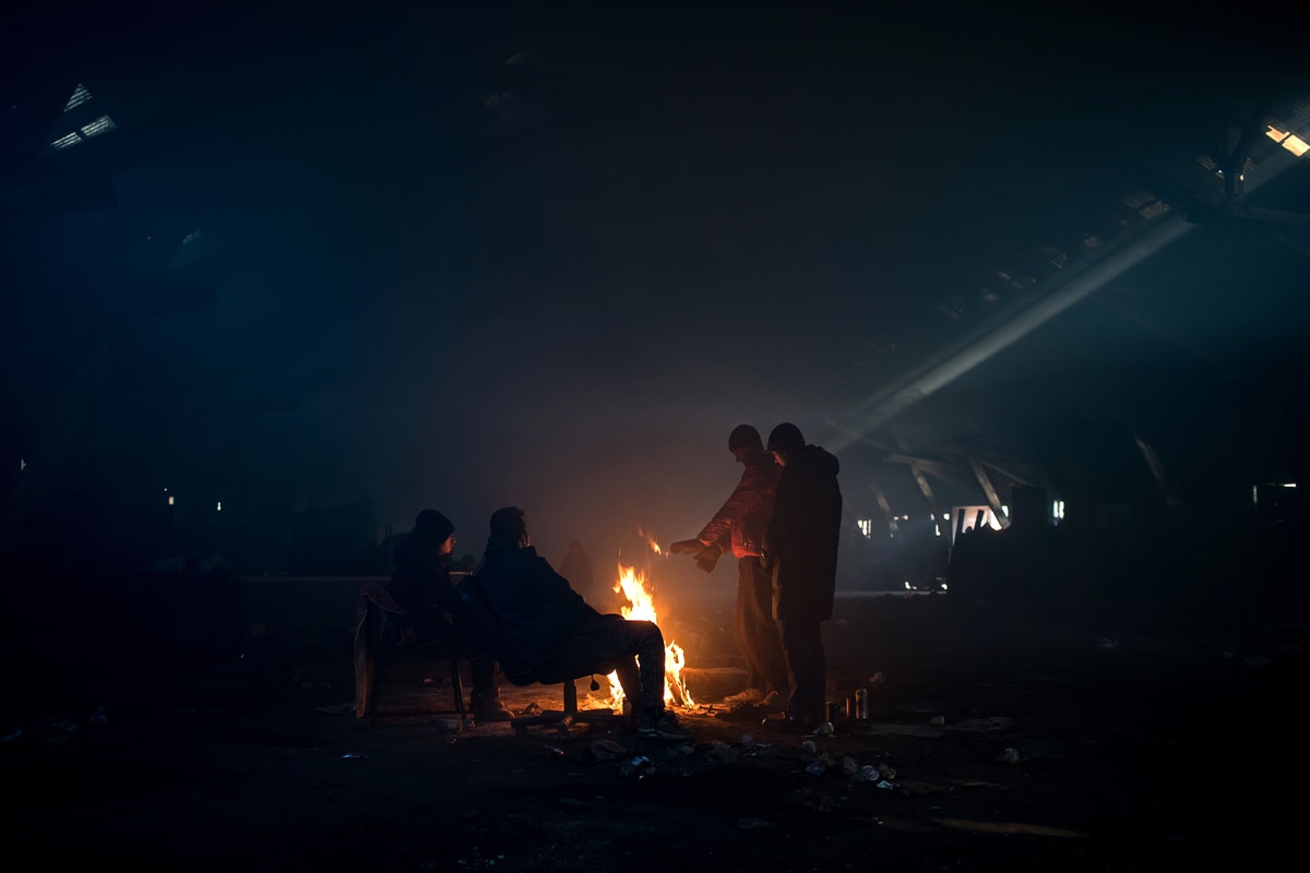 Migrants warm up around a fire inside a derelict warehouse used as a makeshift shelter in Belgrade on January 15, 2017, with temperatures just bellow zero Celsius overnight.