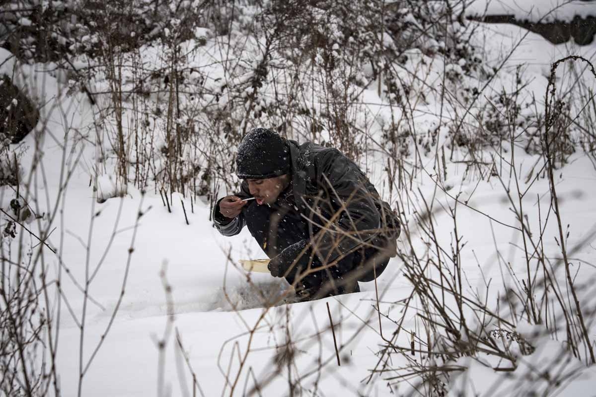 A migrants eats his meal while sitting in the snow in Belgrade on January 11, 2017, as temperatures drop to -15 degrees Celsius in the evening.