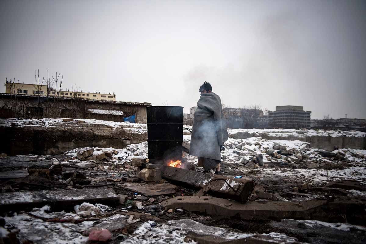 A migrant warms up next to a fire outside a derelict warehouse used as a shelter near Belgrade's main railway station on January 17, 2017, with temperatures bellow zero Celsius. 