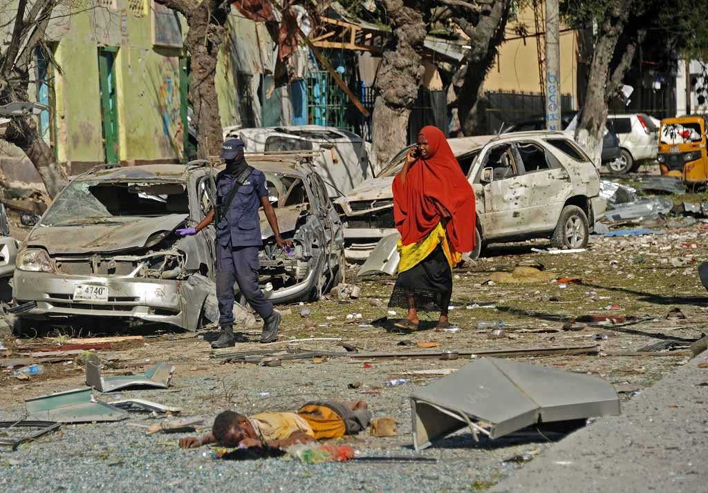 People walk past a dead person on the scene of a terror attack outside The Ambassador Hotel in Mogadishu on June 2, 2016. People walk past a dead person on the scene of a terror attack outside The Ambassador Hotel in Mogadishu on June 2, 2016.
