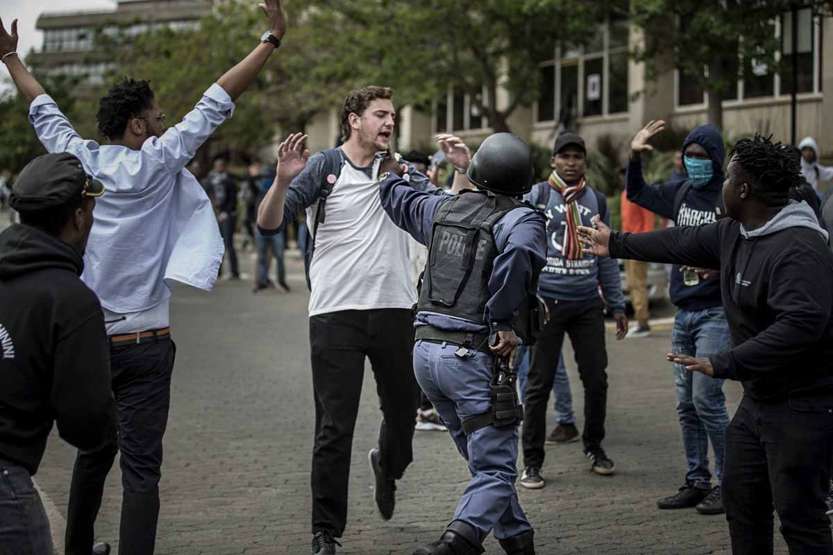 A South African policeman reaches for his weapon in the holster after he was surrounded by University of Witwatersrand students during a running battle with the police forces on campus during a mass demonstration on October 4, 2016 in Johannesburg. A South African policeman reaches for his weapon in the holster after he was surrounded by University of Witwatersrand students during a running battle with the police forces on campus during a mass demonstration on October 4, 2016 in Johannesburg.