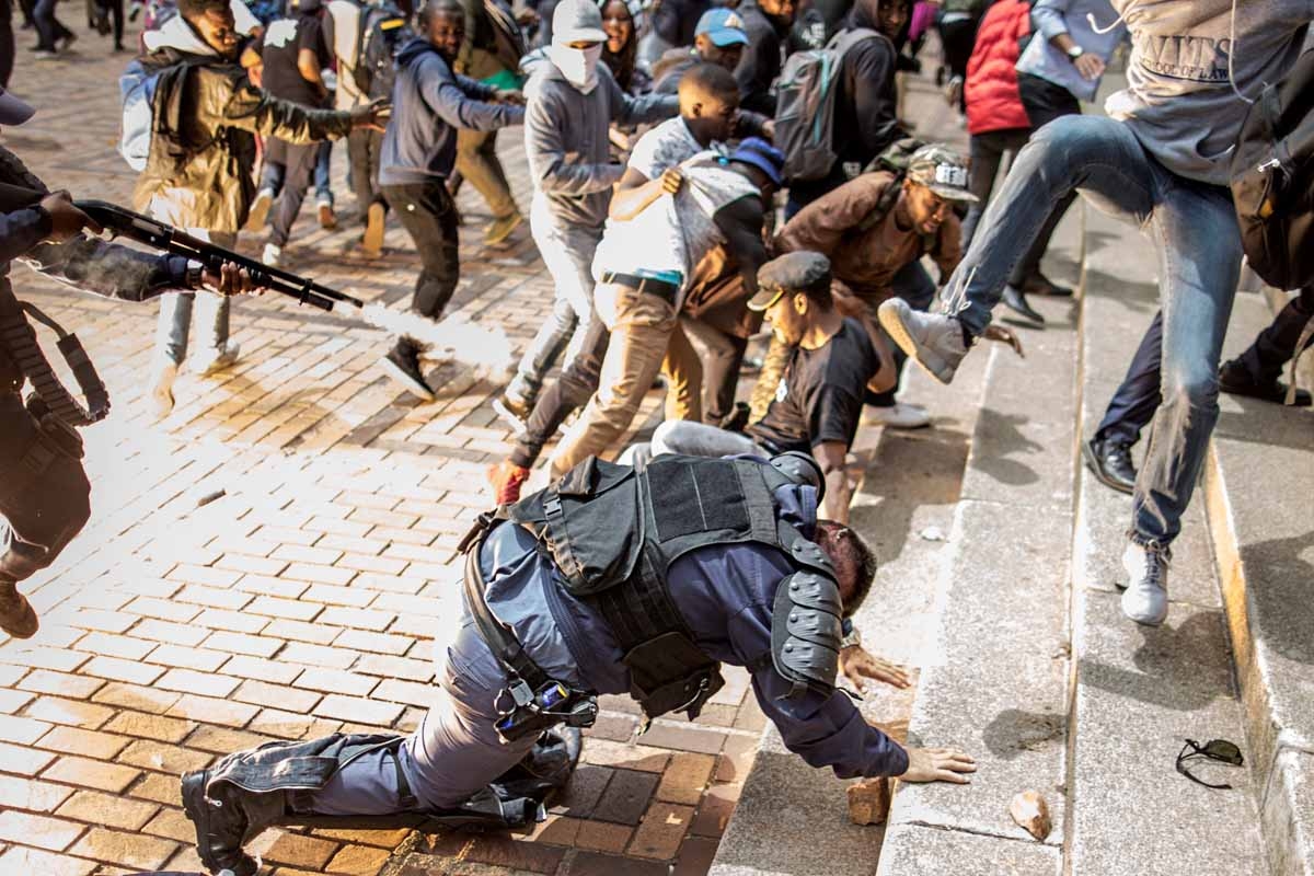 The flash of an exploding stunt grenade is seen while an University of Witwatersrand student jumps on a falling policeman while another policeman discharged his rubber bullet loaded rifle during a running battle with the police forces on campus during a m The flash of an exploding stunt grenade is seen while an University of Witwatersrand student jumps on a falling policeman while another policeman discharged his rubber bullet loaded rifle during a running battle with the police forces on campus during a m