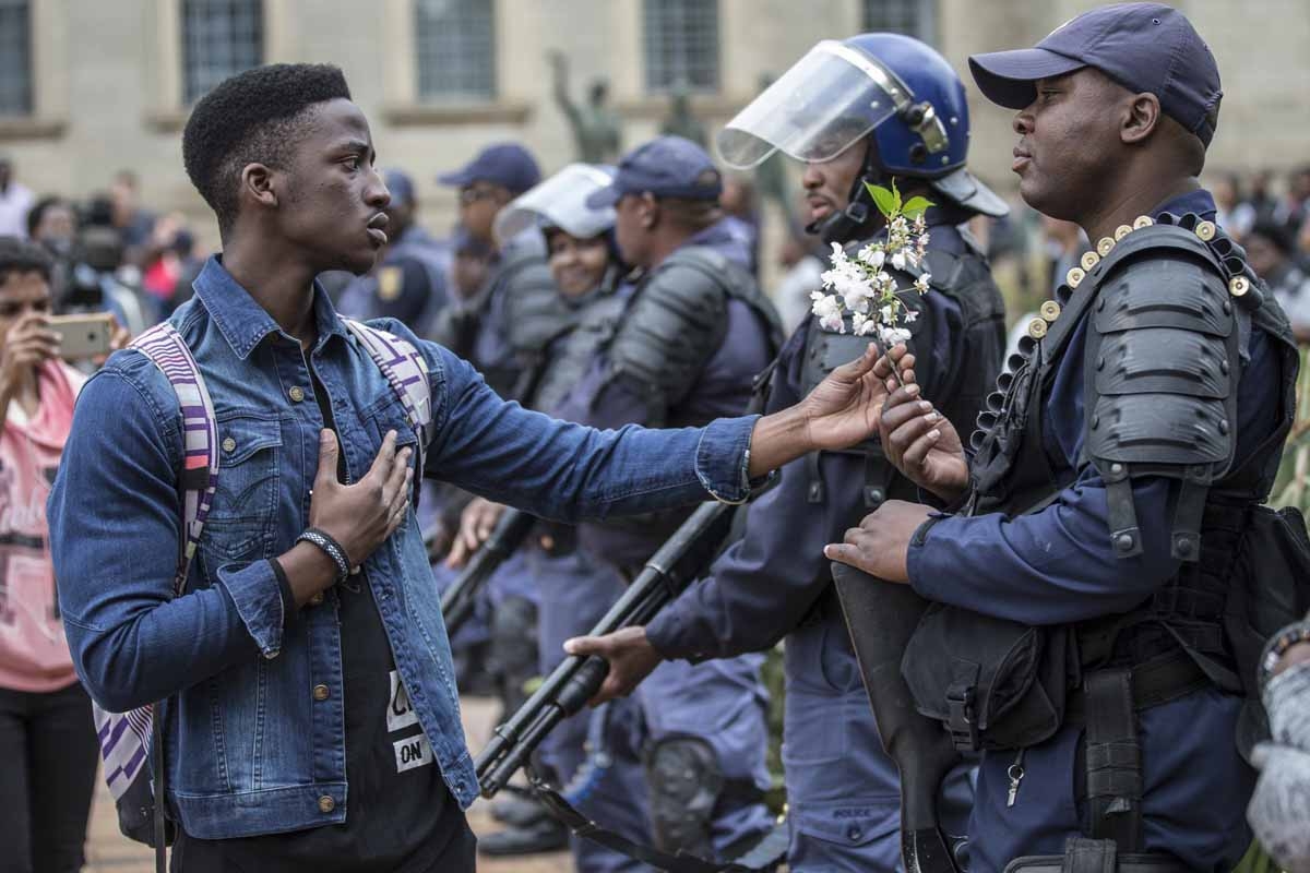 A student at the University of Witwatersrand offers flowers to South African anti-riot policemen during a running battle with the police forces on campus during a mass demonstration on October 4, 2016 in Johannesburg. A student at the University of Witwatersrand offers flowers to South African anti-riot policemen during a running battle with the police forces on campus during a mass demonstration on October 4, 2016 in Johannesburg.