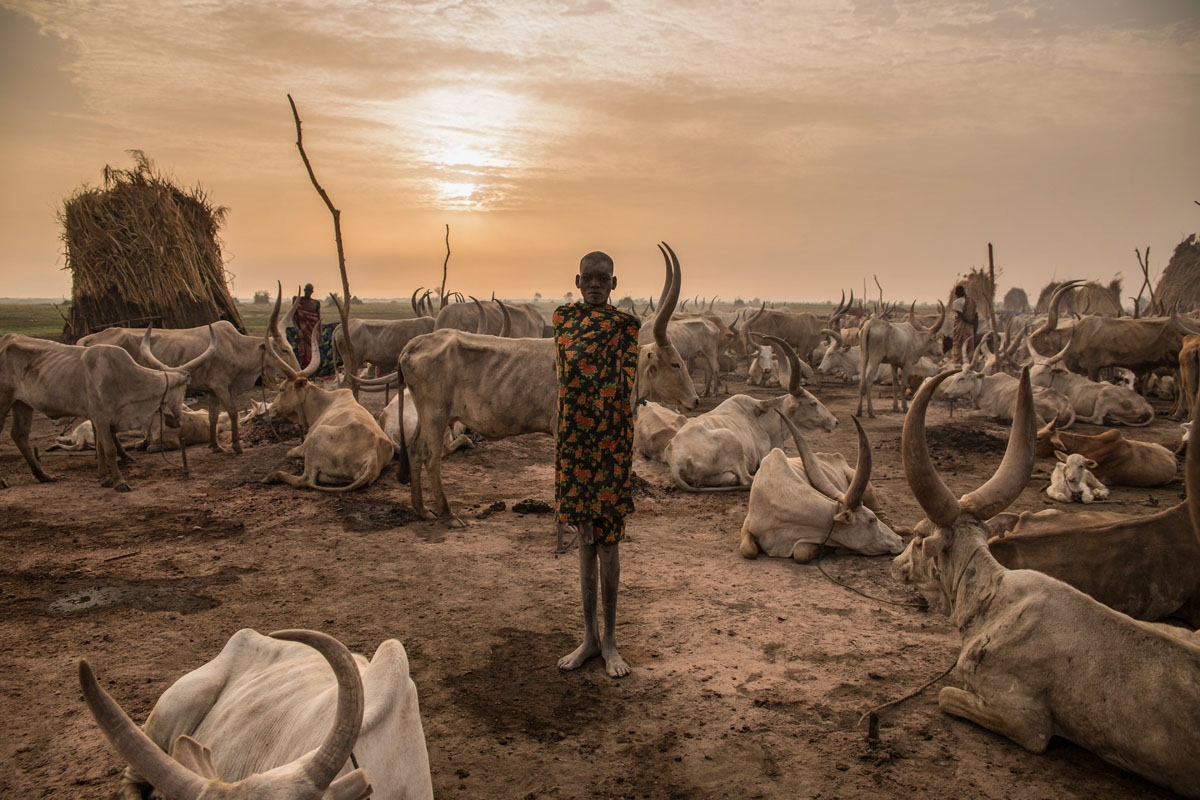 Sudanese girl Den, (14) from Dinka tribe who works as a cattle keeper, cook and cleaner and aid to her brother without attending any school poses at their cattle camp in Mingkaman, Lakes State, South Sudan on March 3, 2018.