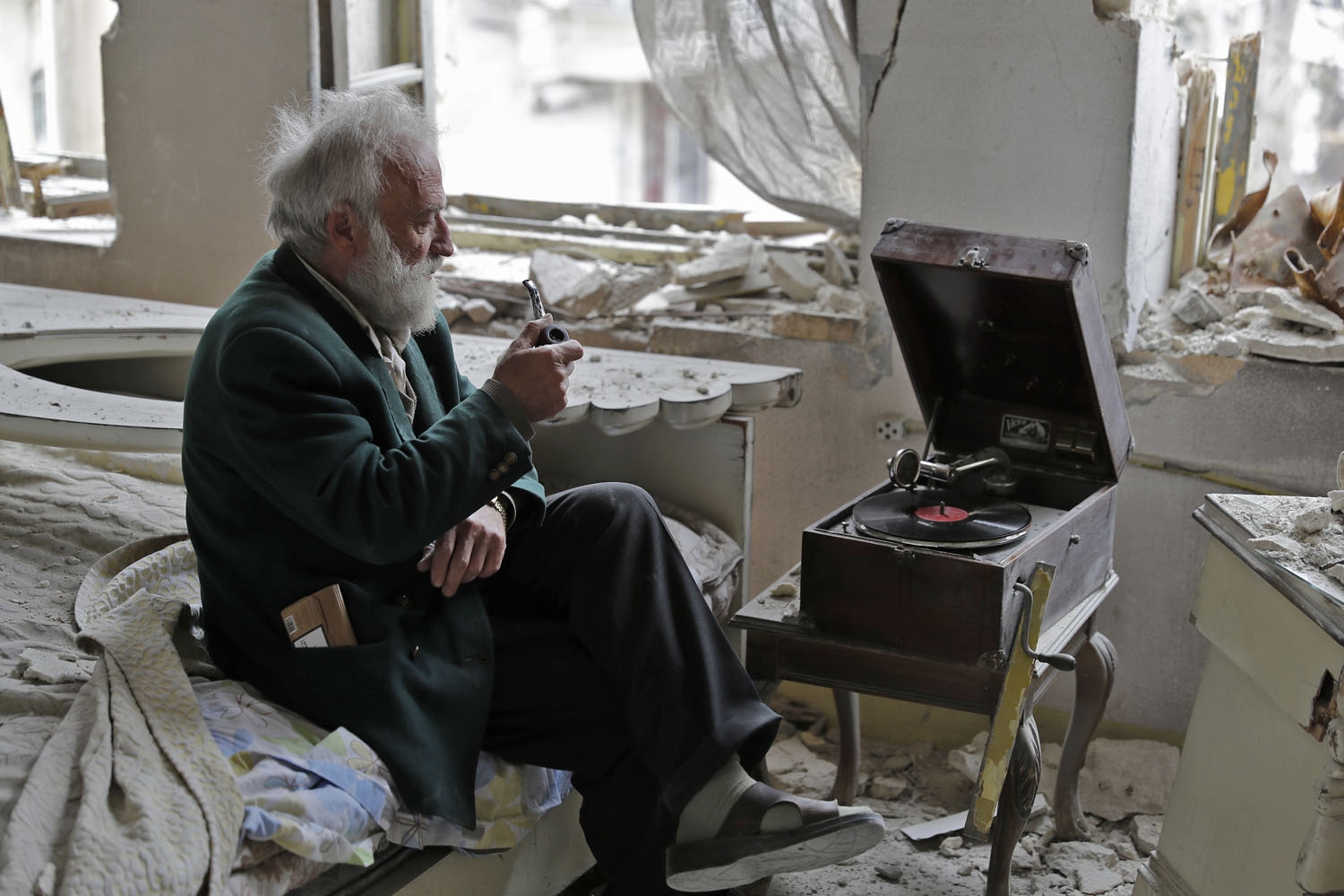 Mohammad Mohiedine Anis, 70, smokes his pipe as he sits in his destroyed bedroom listening to music on his vinyl player, gramophone, in Aleppo's formerly rebel-held al-Shaar neighbourhood on March 9, 2017. / AFP PHOTO / JOSEPH EID