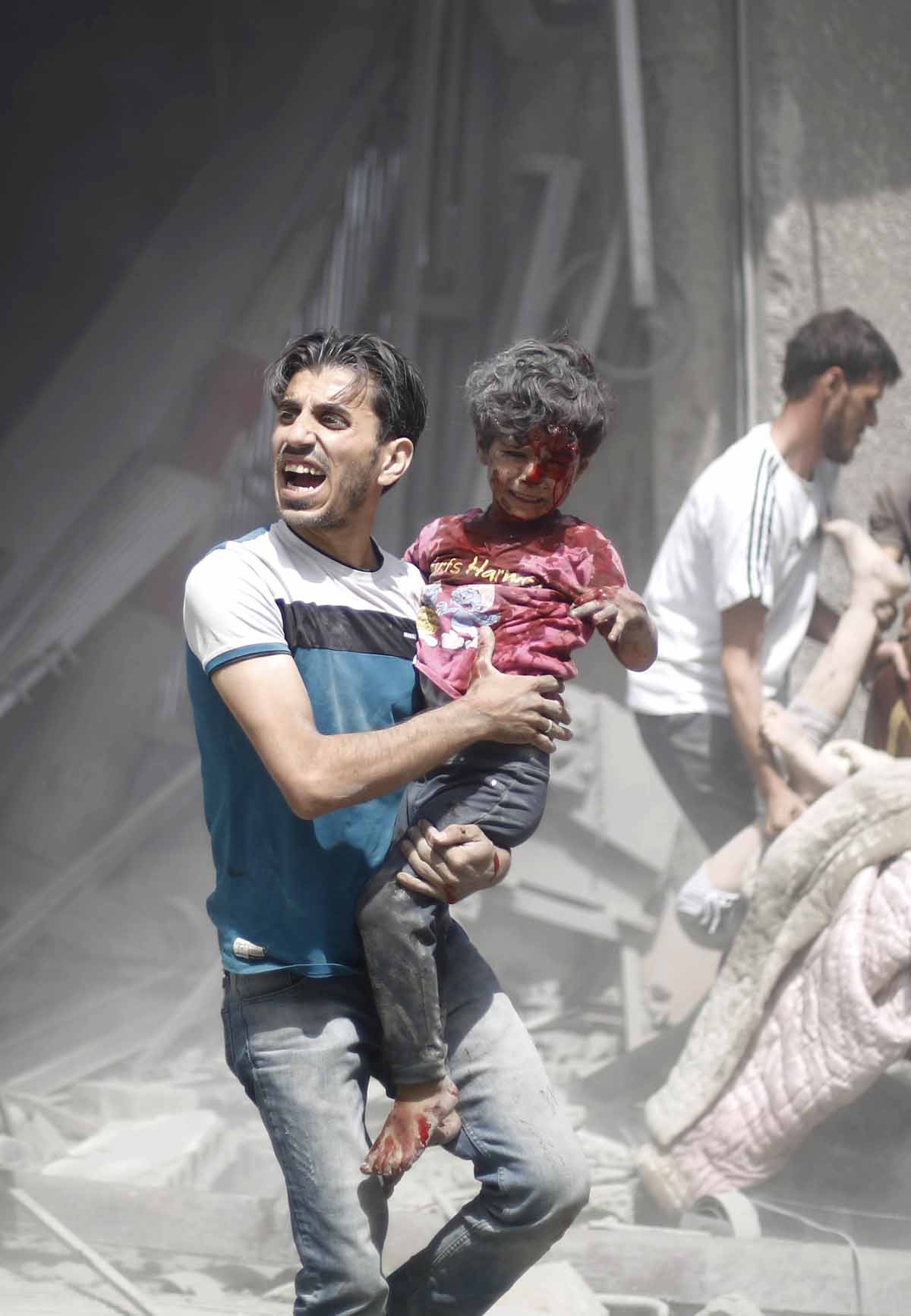 A Syrian man carries a wounded child following a reported air strike by Syrian government forces in the rebel-held area of Douma, east of the capital Damascus, on August 30, 2015.