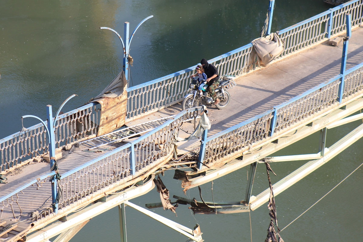 A rebel fighter and a child cross a damaged bridge in Syria's eastern town of Deir Ezzor, on September 2, 2013.