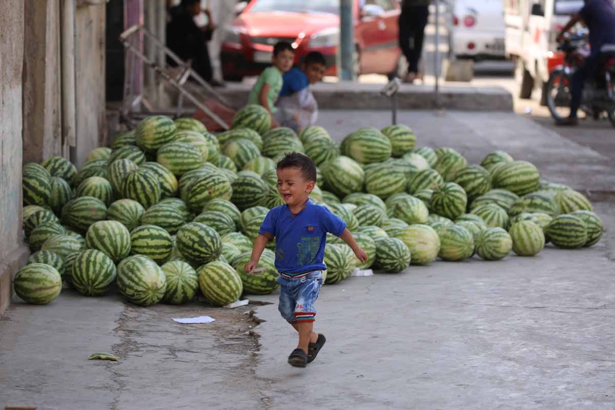 A Syrian child walks past watermelons displayed for sale along on a street in the Kurdish-majority northeastern city of Qamishli on September 16, 2016