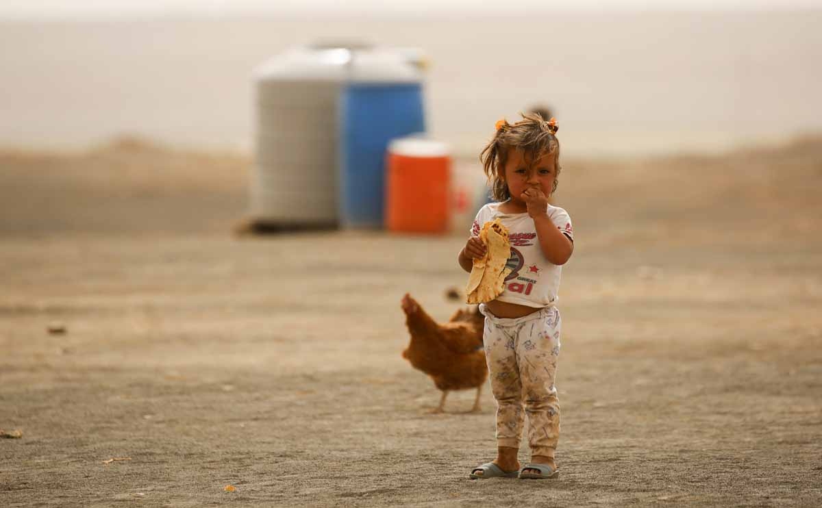 A displaced child, who fled from the Islamic State (IS) group bastion of Raqa, stands outside as she eats a loaf of bread in a camp for displaced near the town of al-Karamah, 26 kms from Raqa, on May 10, 2017. 