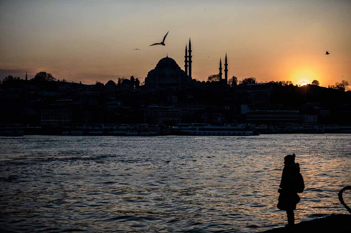 A woman stands on the shore of the Bosphorus river's Golden Horn at Karakoy district as the Suleymaniye Mosque silhouettes against the evening sky, in Istanbul on January 25, 2016.