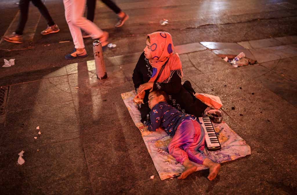 A Syrian refugee woman sits as a child sleeps near her early in the morning on Taksim Square, Istanbul, on May 26, 2015. 