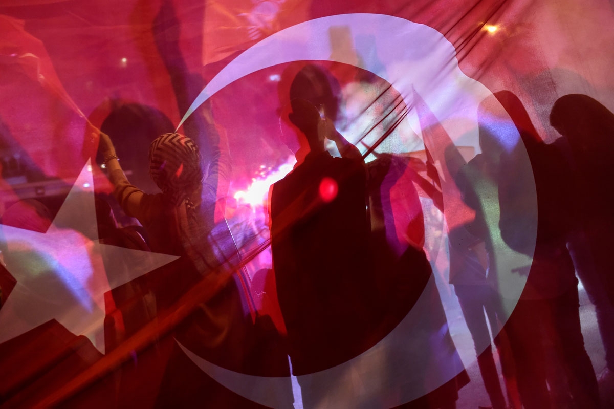 Silhouettes are seen through a Turkish flag as people react outside the Justice and Development Party (AKP) headquarters in Istanbul, on June 24, 2018, during the Turkish presidential and parliamentary elections.